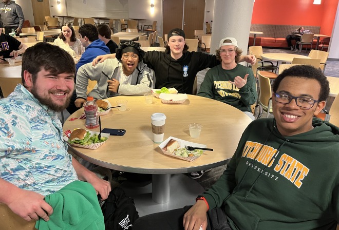 Male students at table in the Falcon Hub eating food