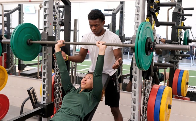 Student bench pressing with a spotter in gym at landry