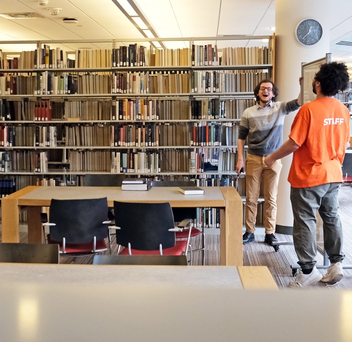Students standing in library having animated discussion in front of the bookcase
