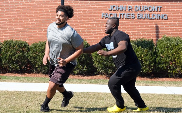 Two male students playing football on quad in front of Dupont