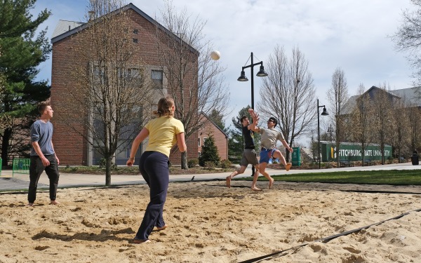 Students playing beach volleyball on campus with Mara and mailboxes in background