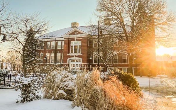 Snowy Percival Hall and Quad with sun shining through trees