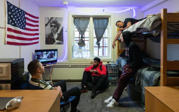 Male students in dorm room on bunkbeds watching tv and talking