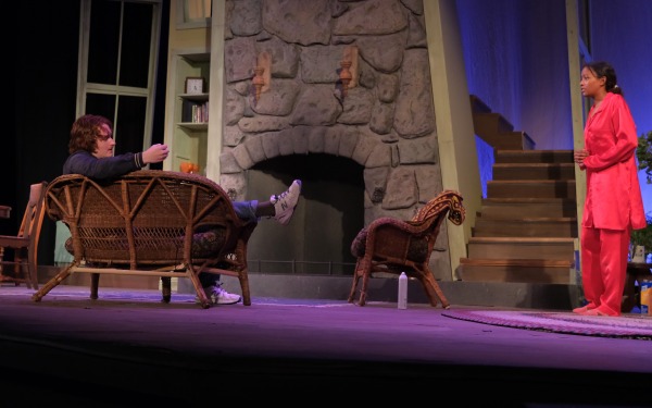 Male and female actors on stage in front of fireplace