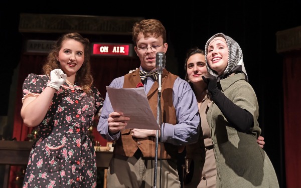 One male and three female actors performing in front of the microphone on stage