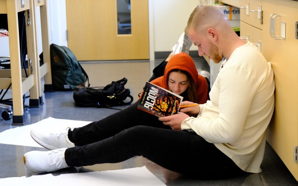 students looking at Bloom book on the floor of a classroom for inspiration for their poster