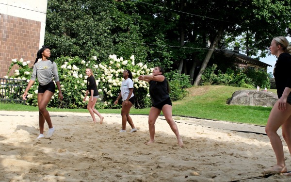 Group of students playing in the sand on the volleyball court on campus