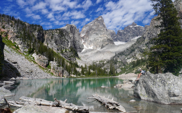 Person sitting on rock by lake with mountains in background.