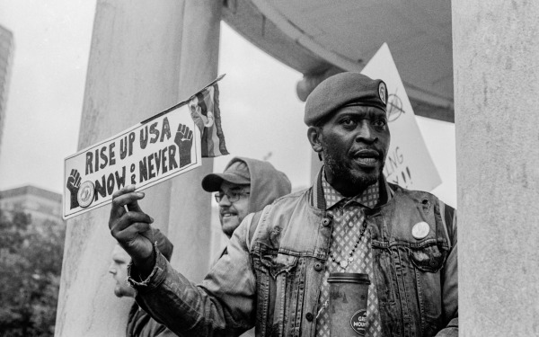 Black and white photo of man with Rise Up USA Now or Never sign.
