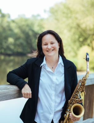 Amy McGlothlin outside with sax leaning against wall.