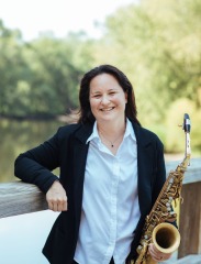 Amy McGlothlin outside with sax leaning against wall. 