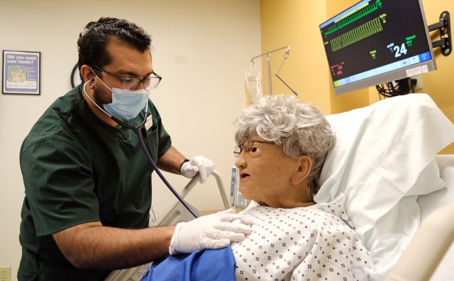 Male nursing student listening to heart of patient in hospital bed