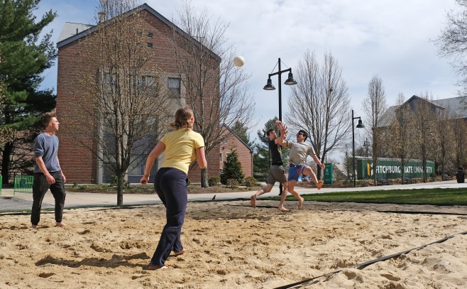 Students playing beach volleyball on campus with Mara and mailboxes in background