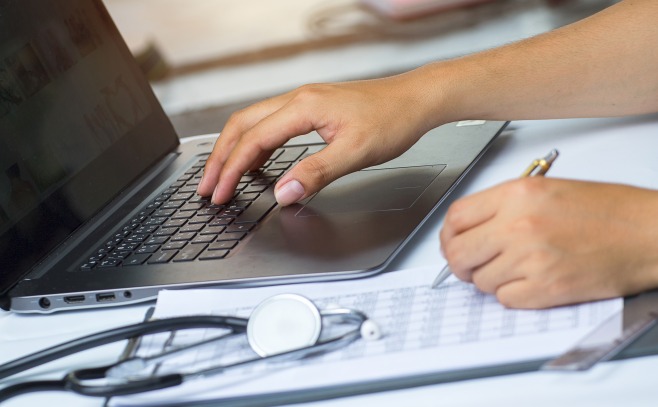 Nursing student hands typing on a laptop with stethoscope next to it