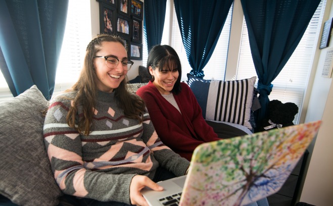 students sit in a dorm sharing a laptop
