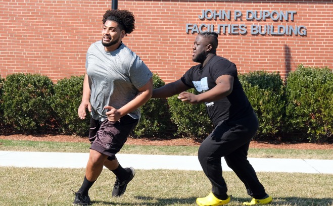 Two male students playing football on quad in front of Dupont