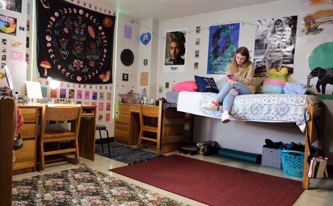 Female student sitting on bed in her dorm room looking at her phone