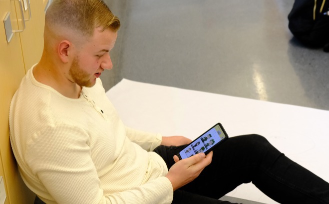 Male student sitting on floor looking at this phone