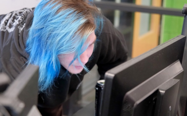 Student with blue hair on desktop computer in classroom