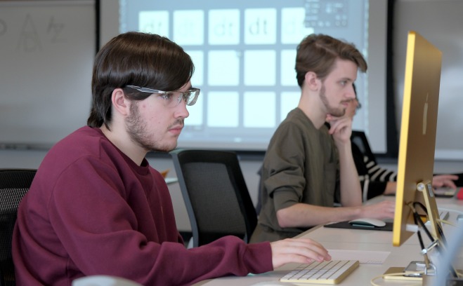 Two male students on computers in communication classroom