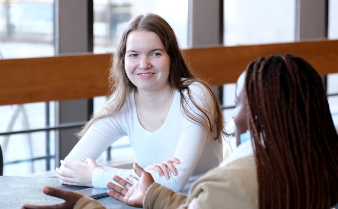 Smiling female students in the main lounge sitting at a table. 