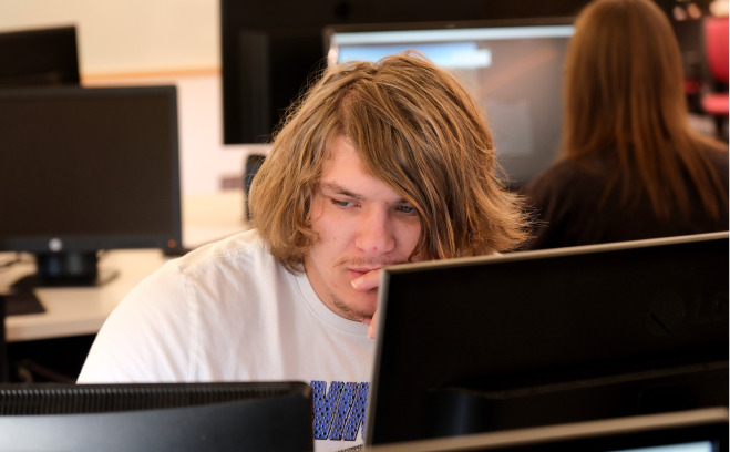 Male student behind computer screens and another student in background