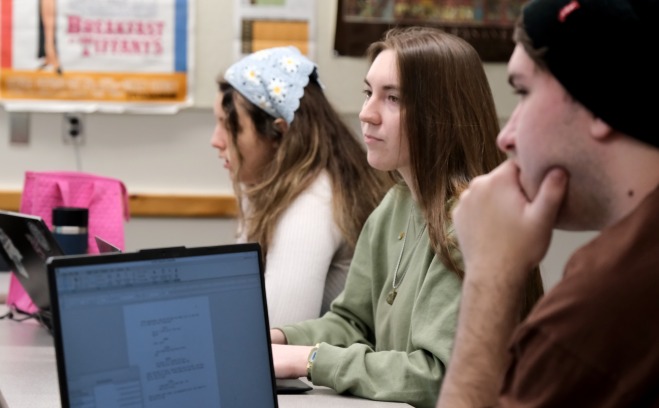 Two female and one male student behind laptops in class