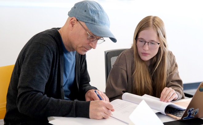 Teacher and student in graphics class at table with papers and laptop