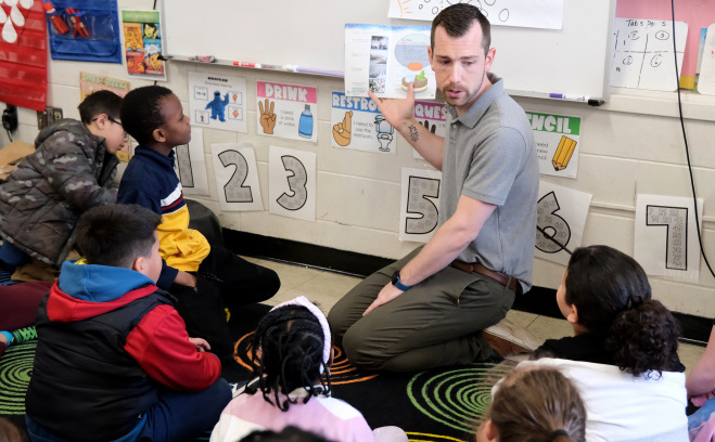 Dustin Halterman in classroom reading to a group of students