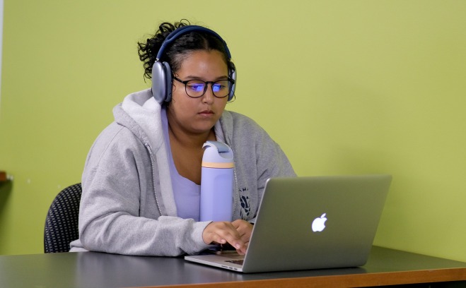 Student on laptop with headphones and water bottle at table in room