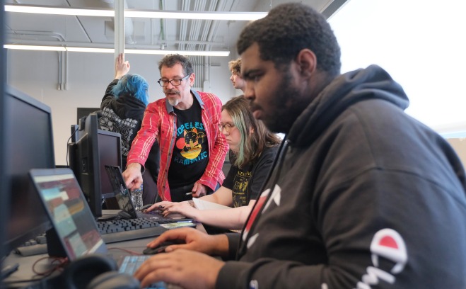 Game design workshop students working on computers with Jeff Warmouth advising