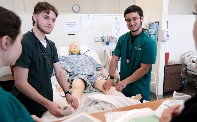 Two male nurses working on mannequin in the bed in lab