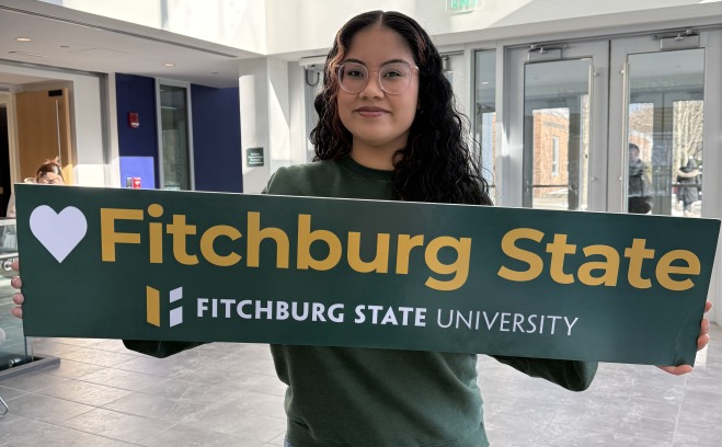 Adriana holding heart Fitchburg State sign in Antonucci lobby