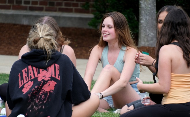 Smiling female students sitting in the grass on quad