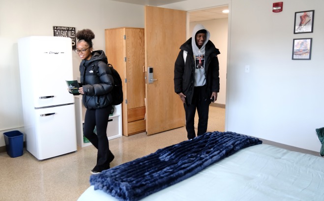 Male and female student walking in room in Herlihy with coats and backpacks