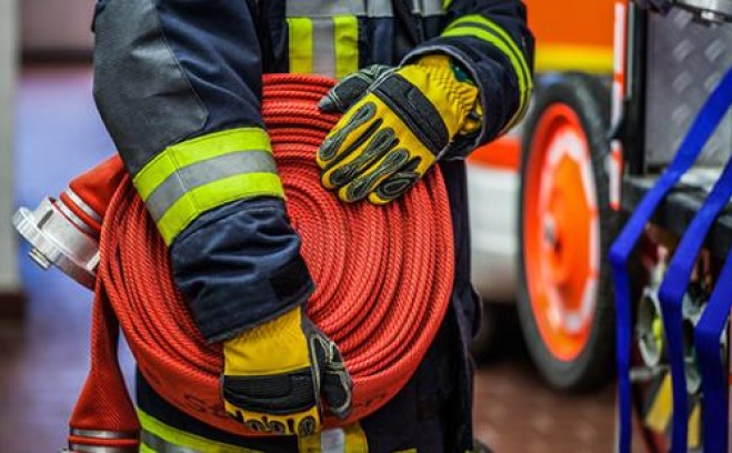 Closeup of firefighters hands holding a hose in front of truck