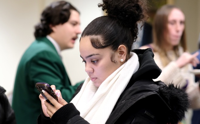 Female student in coat looking at cell phone with students in background