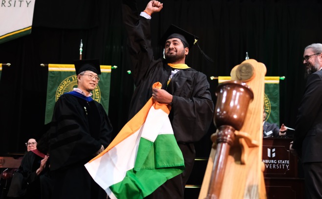 Grad student raising arm in triumph on stage with flag