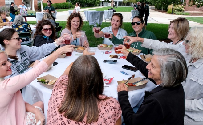 Admin staff on quad at BBQ smiling and raising their glasses in a toast