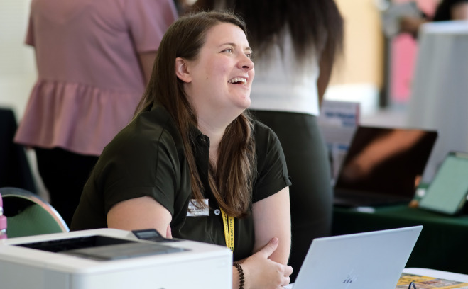 Staff member smiling with laptop at table in Hammond Main Lounge.