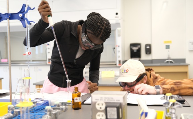 Female and male student pouring chemicals into a beaker in chemistry lab