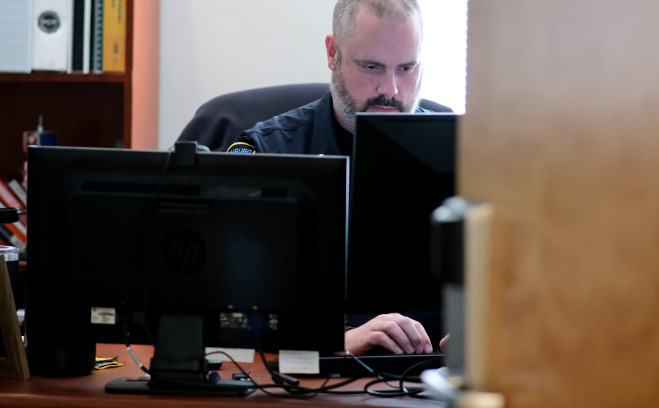 Police officer at his desk behind a computer. 