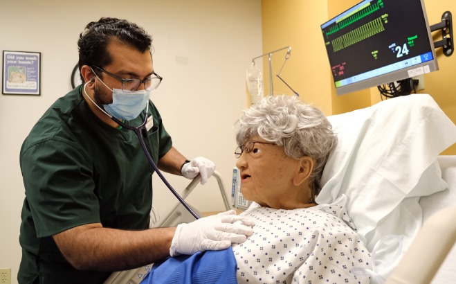 Male nursing student listening to heart of patient in hospital bed