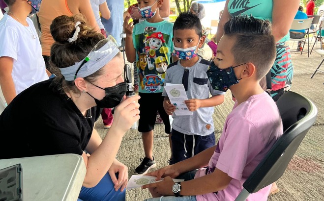 Nursing student checking the eyes of a young boy in Costa Rica while family looks on