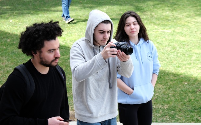 Two male and one female student filming on the quad