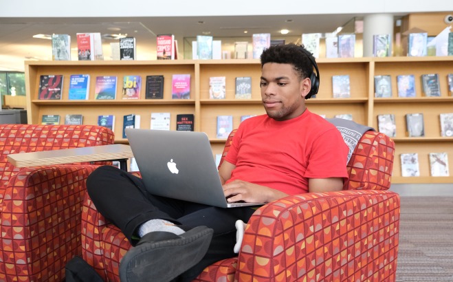 Male student sitting in chair on his laptop in the library