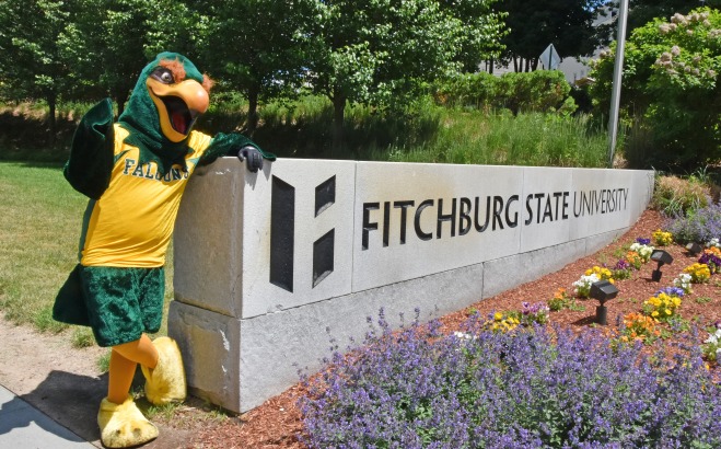 Freddy standing next to Fitchburg State University sign with flowers