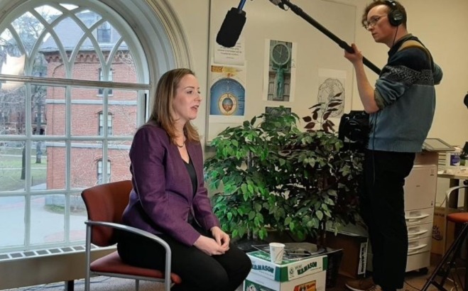 Comm Media Intern on location shoot holding microphone over woman