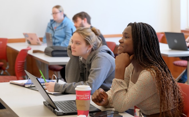 Two female students sitting in a classroom with others in the background