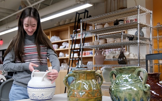 Female student holding and admiring pottery 